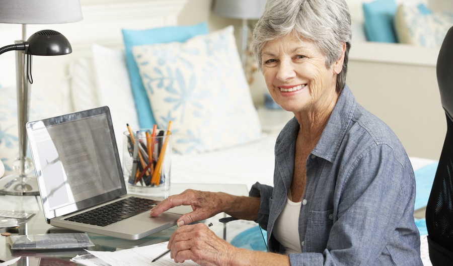 Mulher idosa sorri para a câmera de uma mesa de escritório